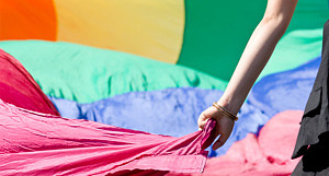 En hand håller i en rosa flagga. I bakgrunden syns fler flaggor i regnbågsfärger.