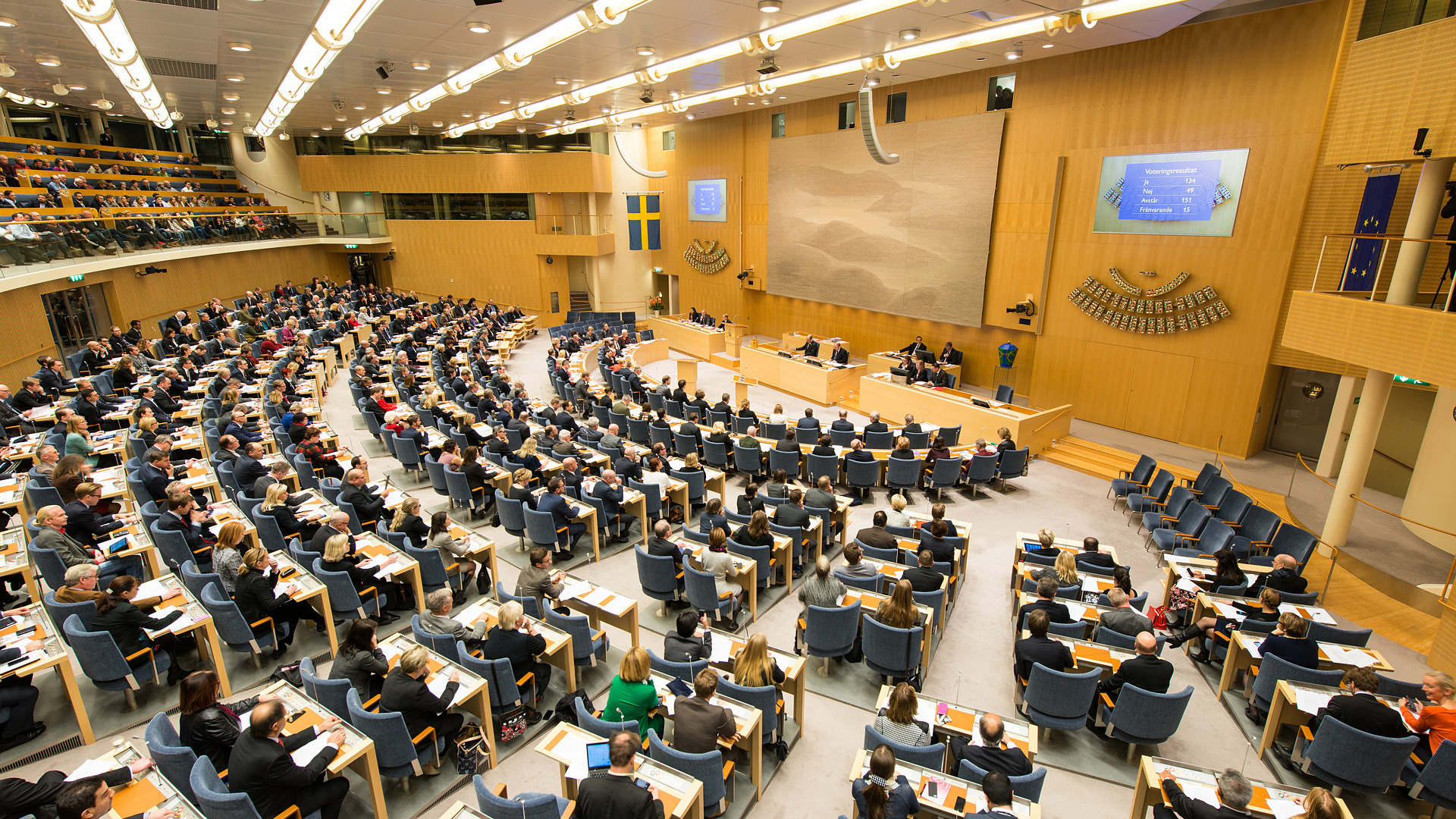 Panoramabild över plenisalen i riksdagen. Ledamöter sitter i sina bänkar.
